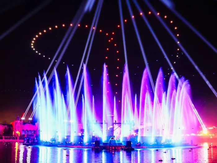 Jets d’eau illuminés en bleu et rose et faisceaux laser au-dessus du lac lors de Disney Cascade of Lights.