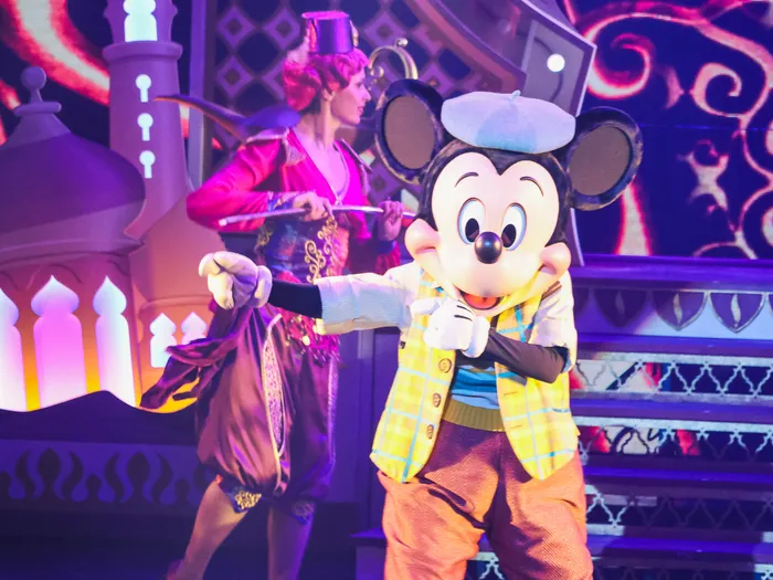 Mickey en gilet jaune et béret bleu s’avance sur scène devant un décor d’Aladdin, spectacle Mickey et le Magicien