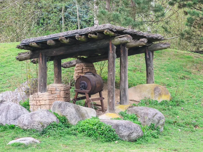 Vieille baratte en bois sous un abri de rondins entouré de rochers, décor pionnier près du dépôt de Frontierland.