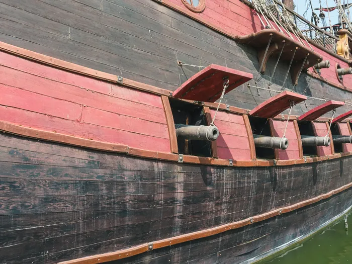 Flanc rouge et noir du galion des pirates avec ses canons alignés aux sabords, au bord de l’eau à Adventureland.
