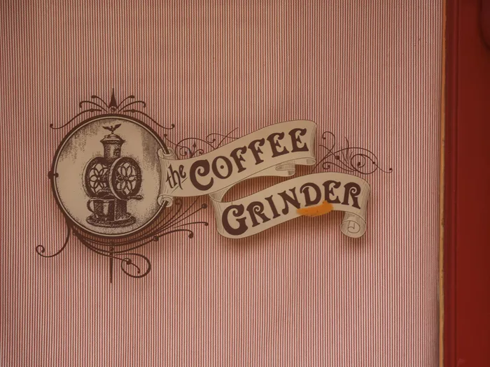 Enseigne rétro « The Coffee Grinder » avec moulin à café dessiné, sur un mur rayé rose du kiosque de Main Street.