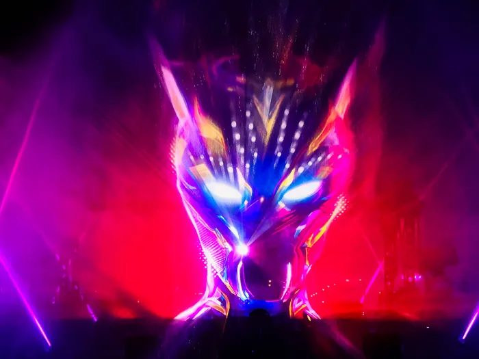 Visage stylisé projeté au-dessus de l'eau entre des faisceaux lasers rouges et bleus, spectacle nocturne
