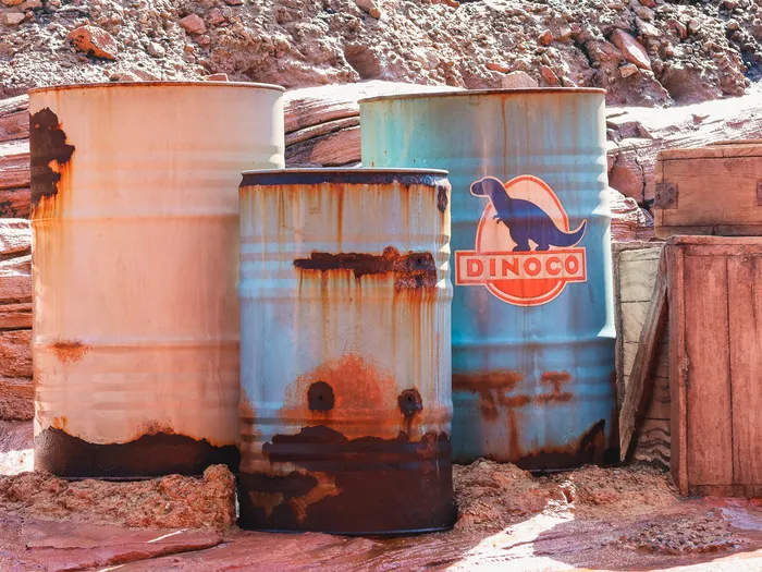 Barils rouillés dont un au logo Dinoco et caisse en bois posés sur des rochers rouges du décor Cars.