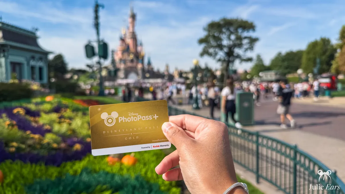 Gold Disney PhotoPass+ "Disneyland Pass Gold" card held in a hand in front of Sleeping Beauty Castle, at Disneyland Paris