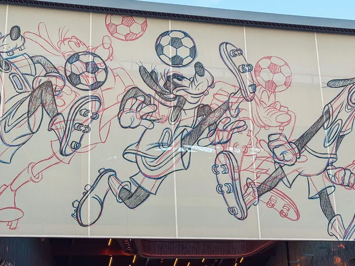 Fresque murale du Sports Bar au Disney Village montrant Dingo en croquis bleus et rouges jouant au football.