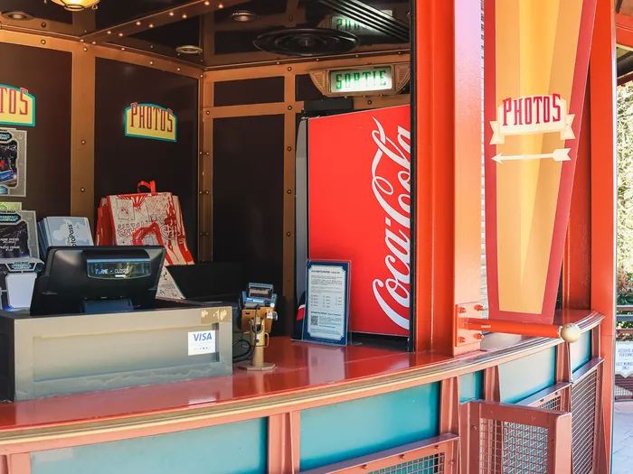 Service counter and till under the "Photos" signs of Light Speed Photography, with a Coca-Cola fridge, at Disneyland Paris.
