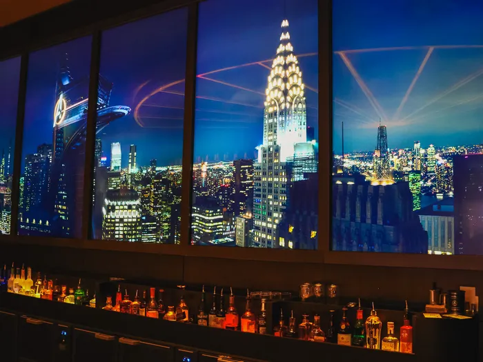 Fresque lumineuse de la skyline de New York au-dessus des bouteilles, derrière le comptoir du Skyline Bar.