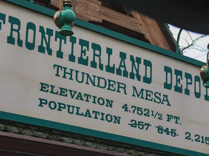 Gros plan de l’enseigne Frontierland Depot indiquant l’altitude et la population fictive de Thunder Mesa à la gare du train