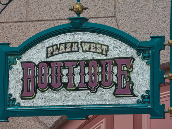 Hanging Plaza West Boutique sign with mauve Victorian lettering on a green frame, at Disneyland Paris