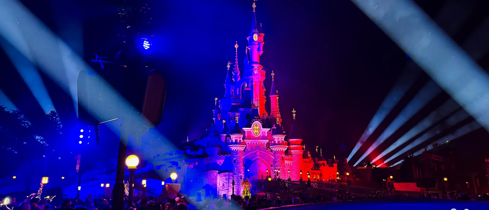 Château illuminé de bleu et de rouge avec faisceaux lumineux pendant le spectacle du 14 juillet à Disneyland Paris