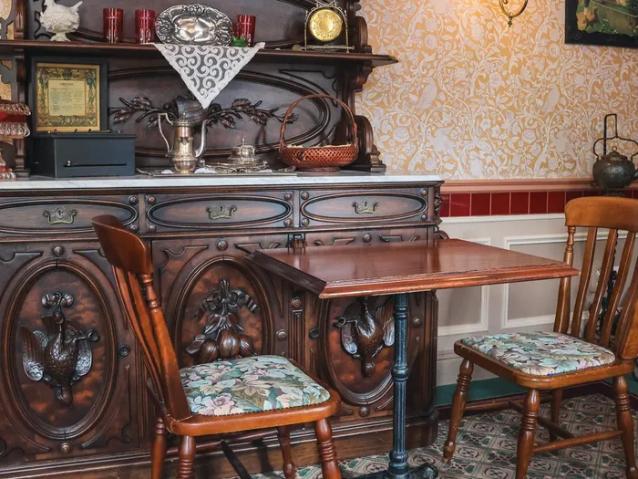 Buffet en bois sculpté, table et chaises à assise fleurie devant un papier peint doré, salle de Victoria’s Home-Style Restaurant.