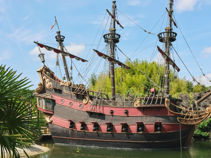 Le galion des pirates amarré sur son plan d’eau entouré de verdure, avec ses trois mâts et sa coque rouge, à Adventureland.