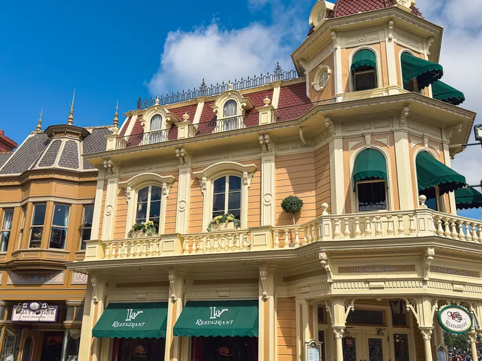 Grande façade victorienne jaune du restaurant Walt’s avec stores verts et enseigne, Main Street USA, ciel bleu.
