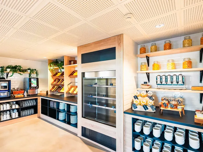 Espace petit déjeuner du Staycity Aparthotel, machines à café, distributeurs de céréales et tasses rangées.