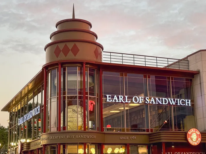 Rotonde vitrée et enseigne Earl of Sandwich aux colonnes rouges, illuminée au coucher du soleil au Disney Village.