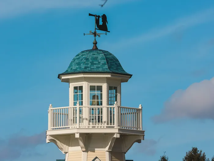 Sommet du phare de l’hôtel Newport Bay Club avec sa girouette nautique sous un ciel bleu.