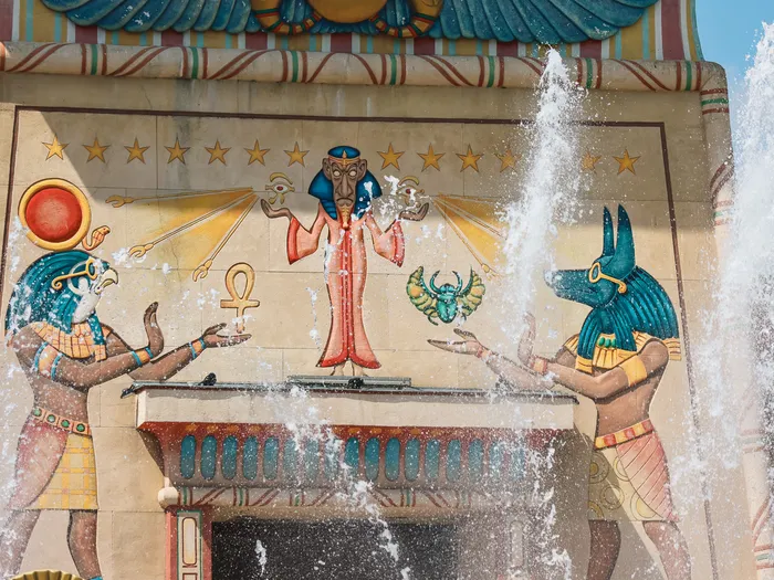 Fresque égyptienne d’OzIris derrière des jets d’eau, Anubis et Horus tendant les mains vers une divinité centrale
