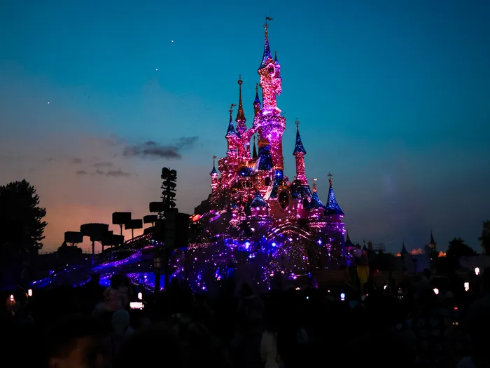 Château de la Belle au Bois Dormant illuminé de rose au crépuscule avant Disney Tales of Magic, Parc Disneyland.
