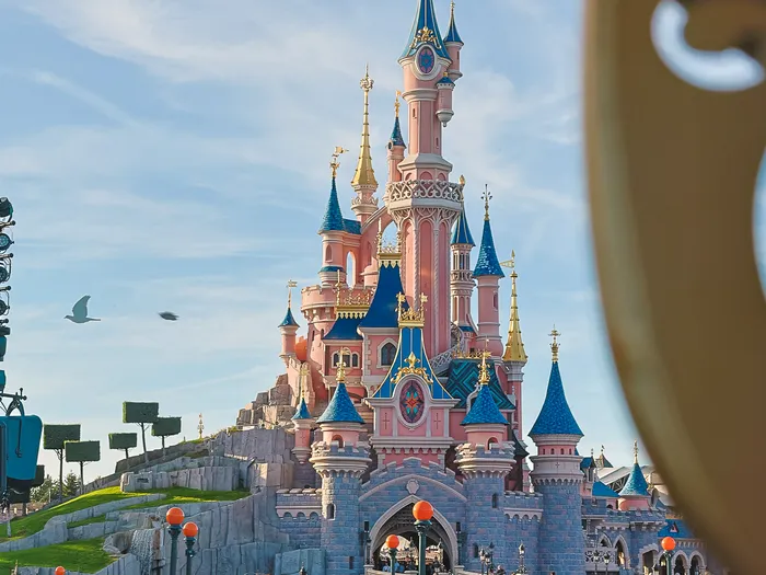 Le château rose et bleu de la Belle au Bois Dormant et ses flèches dorées sous un ciel bleu, Parc Disneyland.