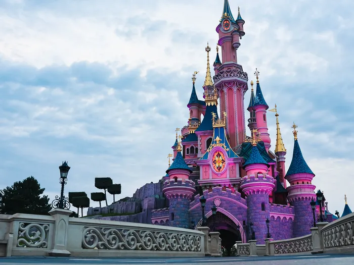 Le château de la Belle au Bois Dormant illuminé de rose face au pont, au crépuscule, à Disneyland Paris
