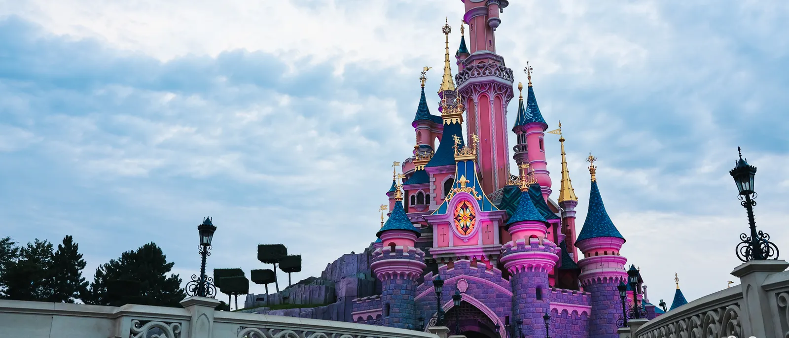 Le château de la Belle au Bois Dormant illuminé de rose face au pont, au crépuscule, à Disneyland Paris