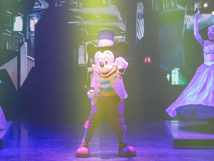 Mickey en costume de magicien avec haut-de-forme entre deux danseuses en robe, spectacle Mickey et le Magicien