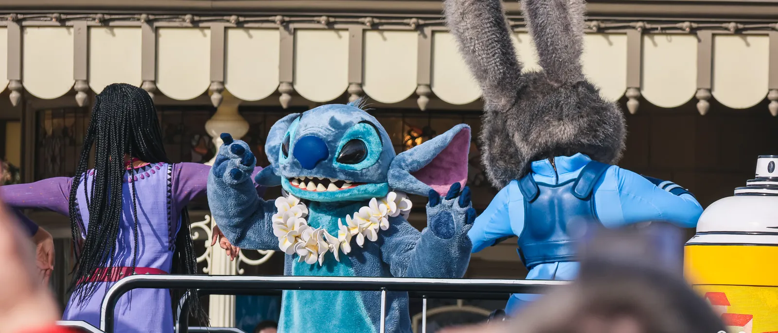 Stitch, un collier de fleurs au cou, lève les bras sur un char de parade à Disneyland Paris