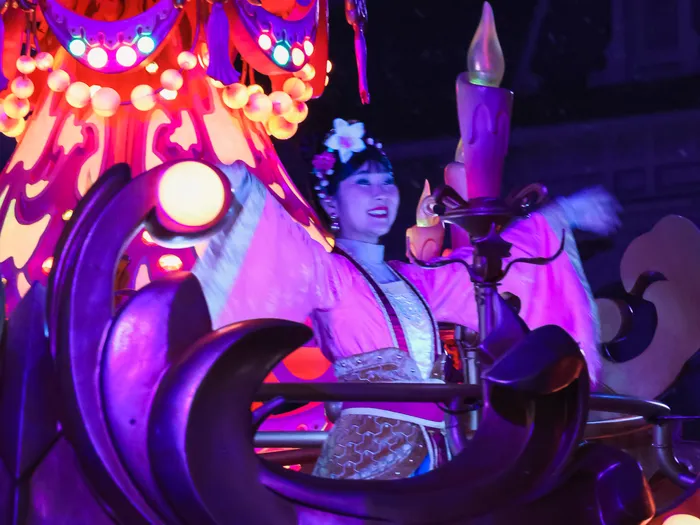 Danseuse en robe rose façon Mulan sur un char aux lanternes violettes et bougies lumineuses pendant la parade de Noël.