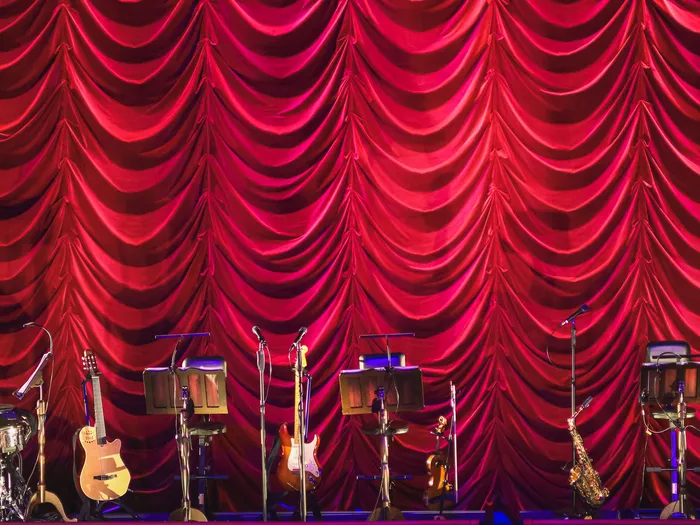 Batterie, guitares, saxophone et pupitres alignés sur la scène de TOGETHER devant un rideau rouge
