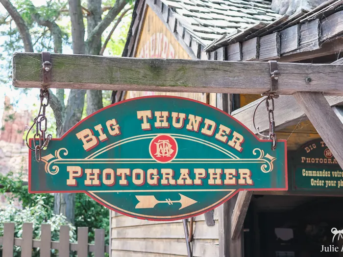 Enseigne en bois vert et rouge Big Thunder Photographer, ornée d’une flèche, près de l’attraction à Frontierland.