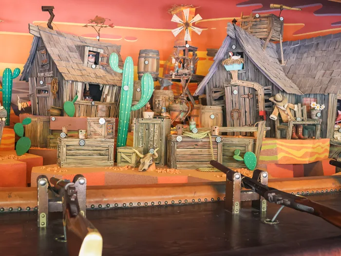 Décor de ville western avec cabanes en bois, cactus et cibles, carabines au premier plan, au Rustler Roundup Shootin’ Gallery.