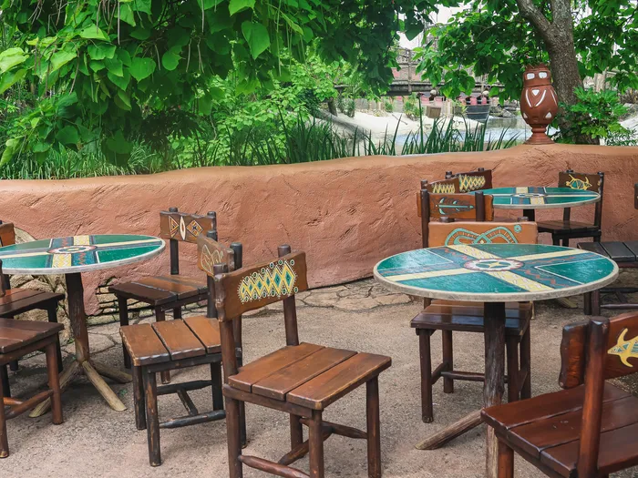 Tables rondes en mosaïque et chaises en bois de la terrasse du Café de la Brousse à Adventureland.