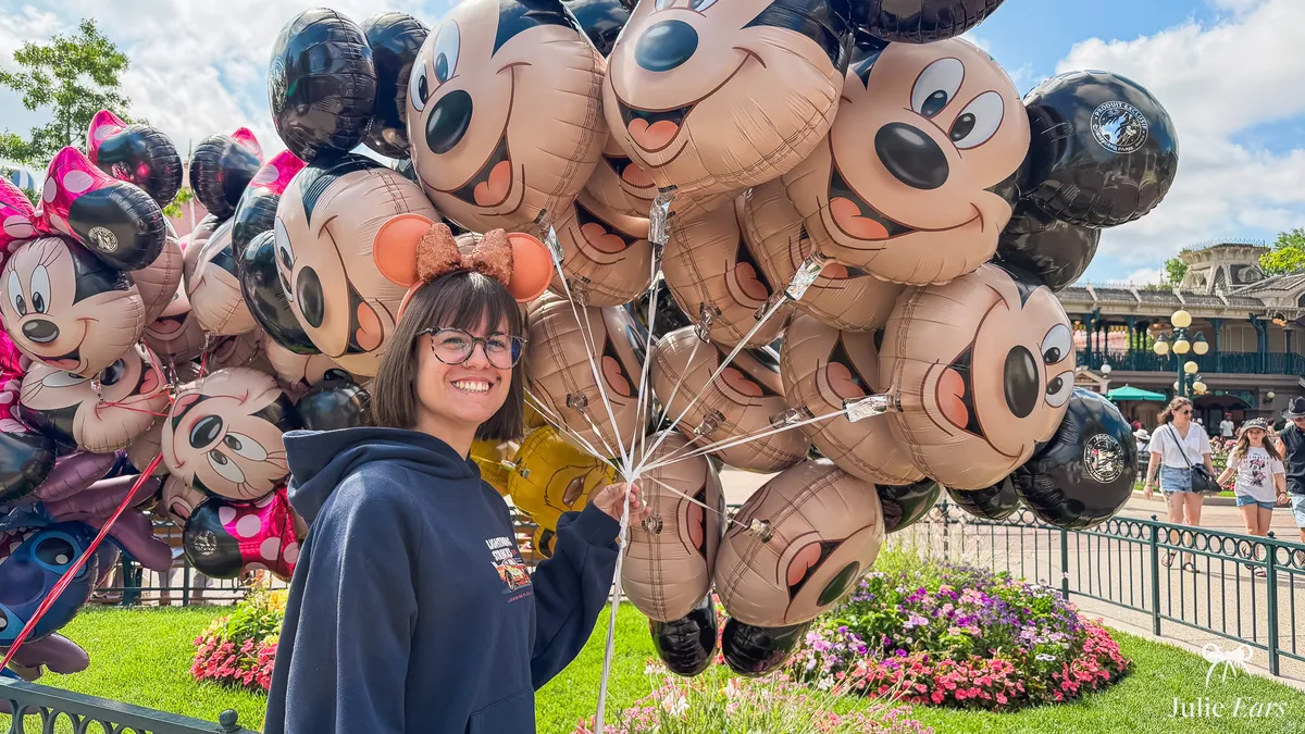 Julie Ears, serre-tête à oreilles de Minnie sur la tête, tient un gros bouquet de ballons en forme de tête de Mickey sur Main Street U.S.A. à Disneyland Paris.