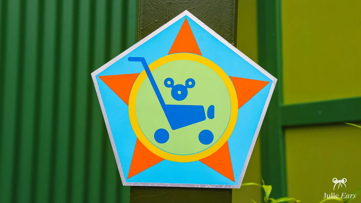 Pentagonal pushchair parking sign at Toy Story Playland, Disney Adventure World: a blue pushchair and a child with a Mickey head on an orange star