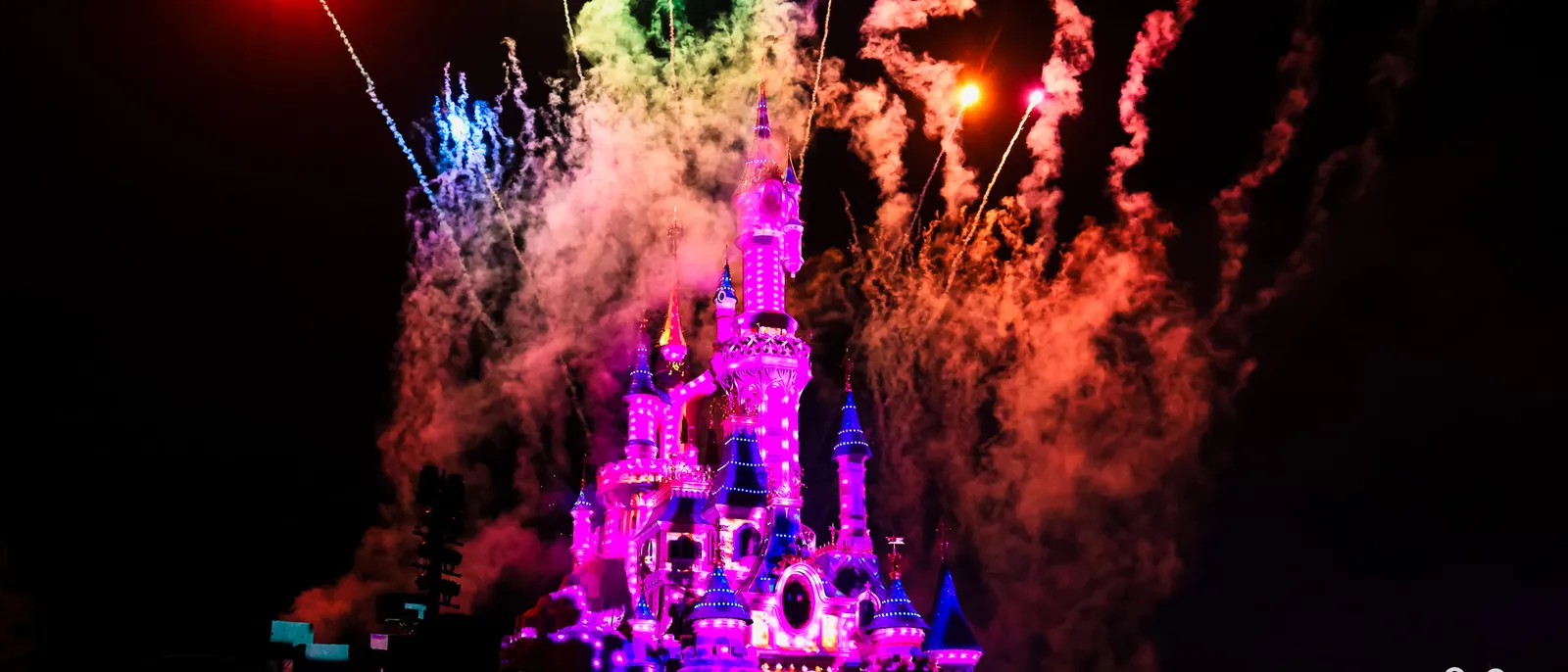 Château illuminé de rose avec feux d’artifice multicolores et fumée dans le ciel nocturne à Disneyland Paris