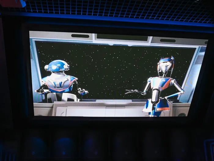 Deux droïdes robotisés face à un hublot étoilé sur un écran de la file d'attente de Star Tours, à Discoveryland