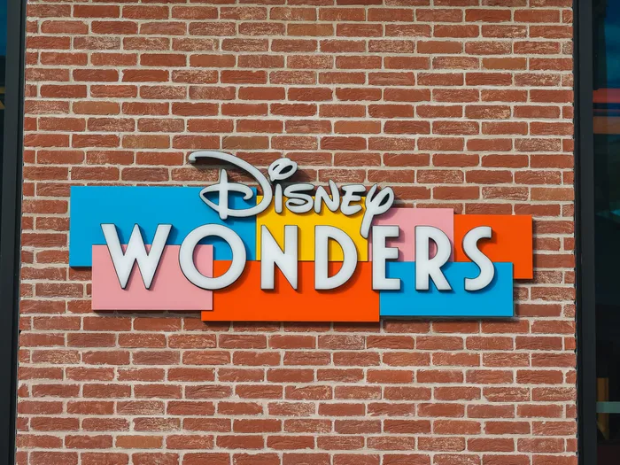 Disney Wonders sign with white letters on colourful rectangles, mounted on a brick wall at Disney Village.