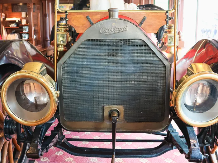 Front of an old "Oakland" car with brass headlamps and wooden-spoked wheels, on display in the Main Street Motors shop at Disneyland Paris