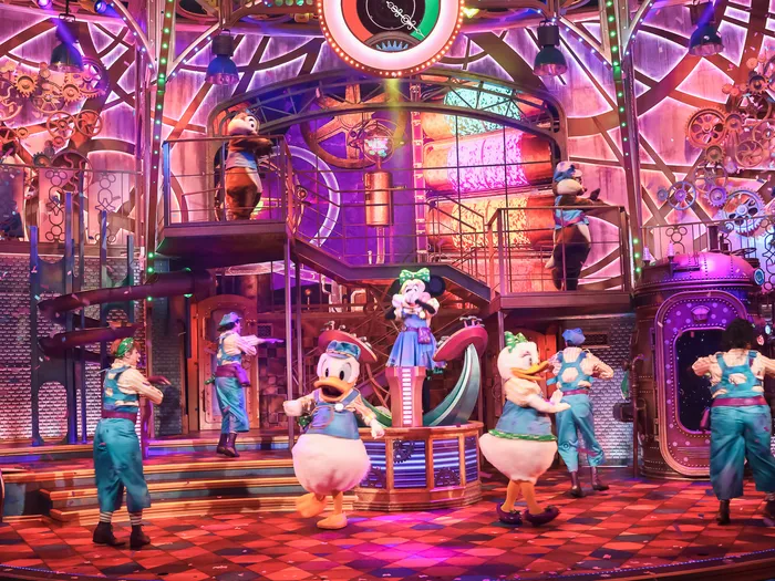 Donald, Daisy et Minnie entourés de danseurs sur le décor d’usine du spectacle Minnie’s Dream Factory.