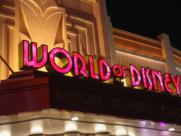 Pink "World of Disney" sign lit up at night on the Art Deco facade.