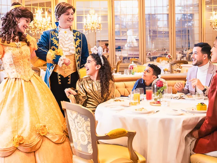 Belle et le Prince saluent une famille à table dans la salle dorée du restaurant La Table de Lumière, Disneyland Hotel.