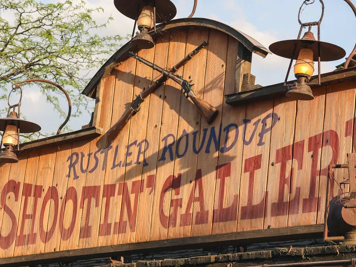 Gros plan sur l’enseigne peinte et les fusils croisés du Rustler Roundup Shootin’ Gallery à Frontierland.