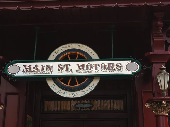 Red facade and entrance of the Main Street Motors shop with its sign and an old Coca-Cola advert above, at Disneyland Paris.