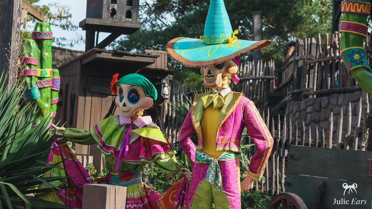 Day of the Dead skeleton couple in the Frontierland Halloween decor: she in a green and pink ruffled dress, he in a pink suit and sombrero
