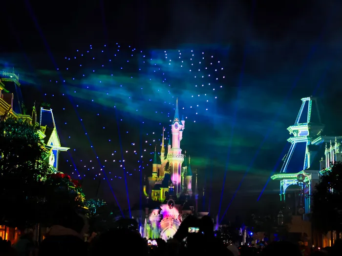 Château éclairé de faisceaux laser bleus et de drones lumineux durant Disney Tales of Magic au Parc Disneyland.
