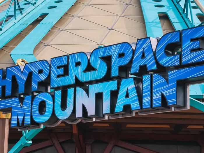 Enseigne bleue Hyperspace Mountain en relief, fixée sur les poutrelles turquoise de l’attraction à Discoveryland.