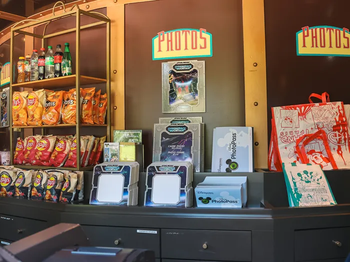 Inside Light Speed Photography at Disneyland Paris: photo frames, PhotoPass kiosks, a souvenir bag and shelves of sweets under the "Photos" sign