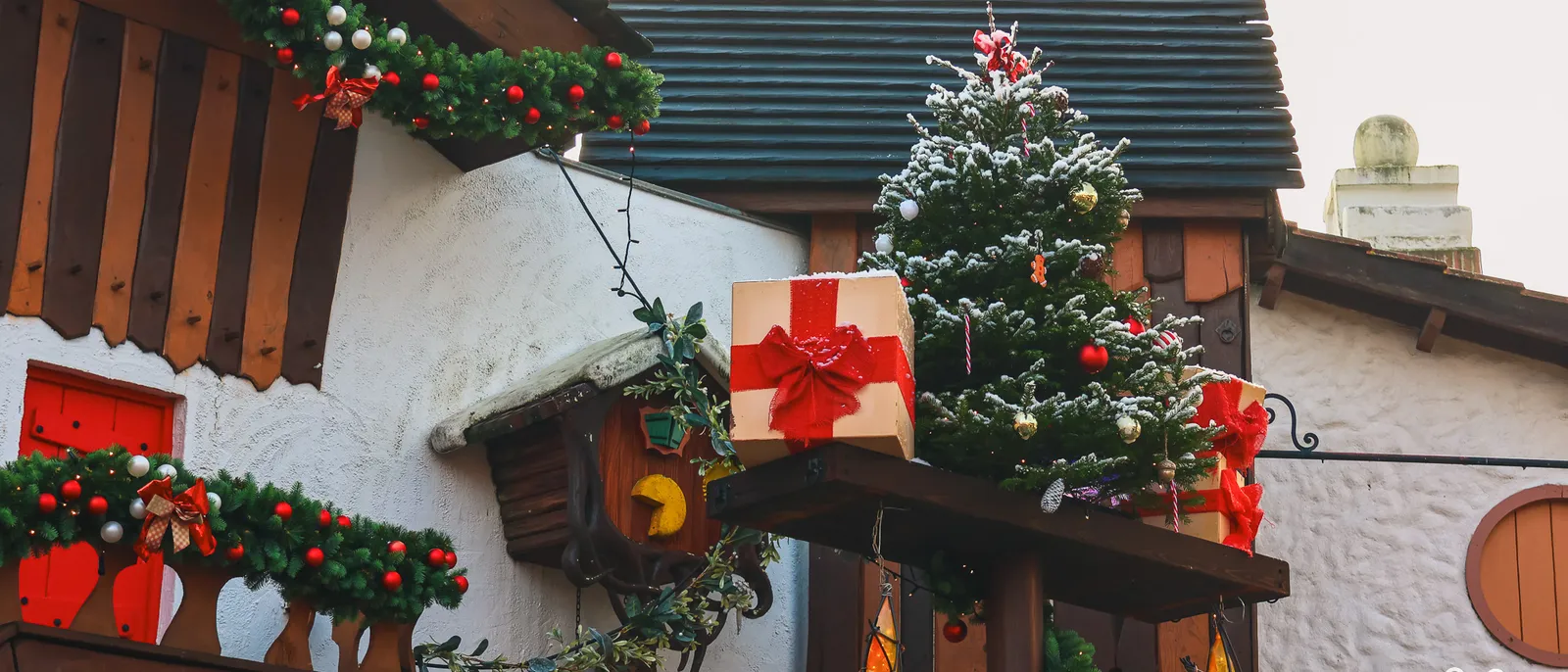 Guirlandes de sapin et nœuds rouges sur les toits en bois du parc, sapin enneigé et paquet cadeau géant en décoration de Noël