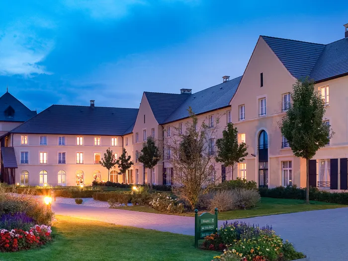 Façade illuminée de l’Explorers Hotel au crépuscule, avec jardins fleuris au premier plan.