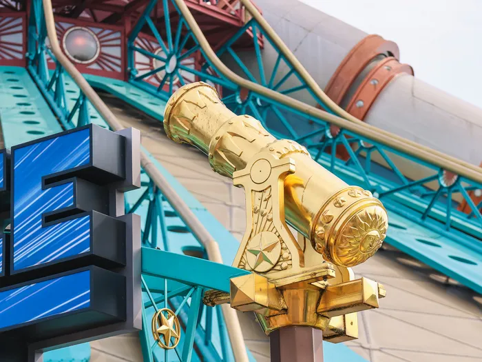 Canon doré ouvragé devant les poutrelles turquoise et le canon central d’Hyperspace Mountain, contre-plongée.